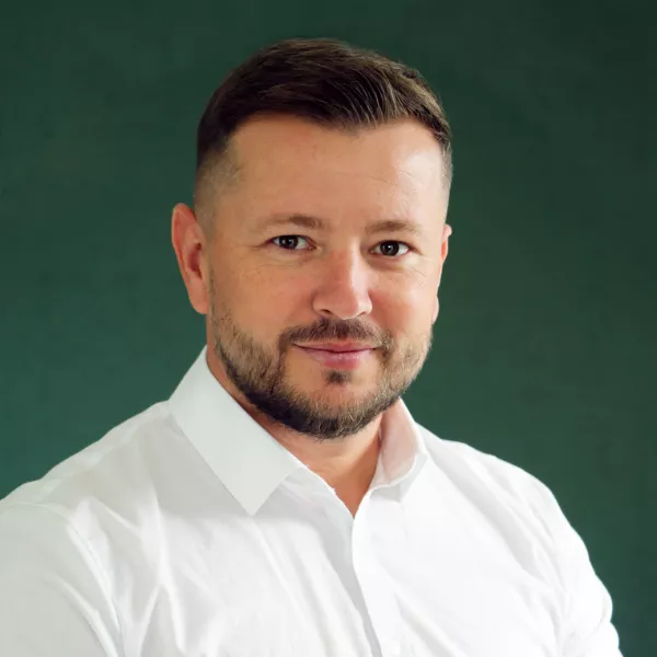 A man wearing a crisp white shirt is posed against a solid green background. The image has a professional and formal tone, suitable for corporate or business contexts. The background is plain, emphasizing the subject's attire and posture.